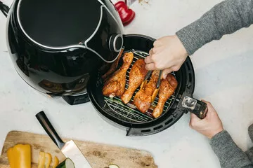 someone flipping food inside the air fryer. The food is chicken drum sticks