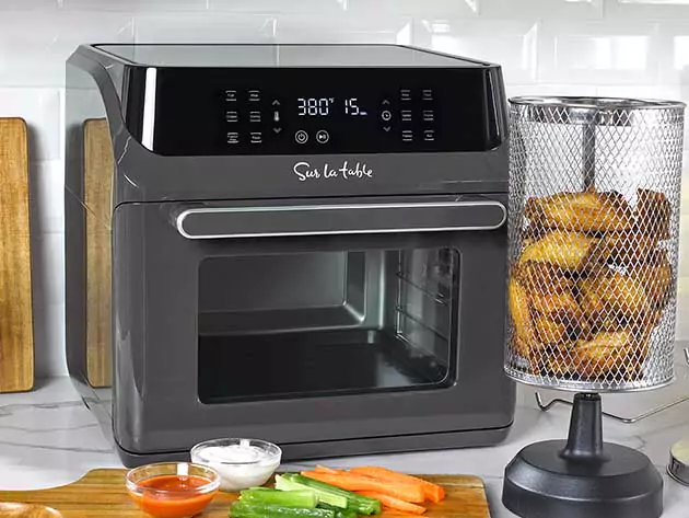 A Sur La Table Air Fryer is displayed on a countertop, with its digital display showing the temperature and time settings. Beside it, there are sliced vegetables and dipping sauces, indicating the air fryer’s use for healthy cooking.
