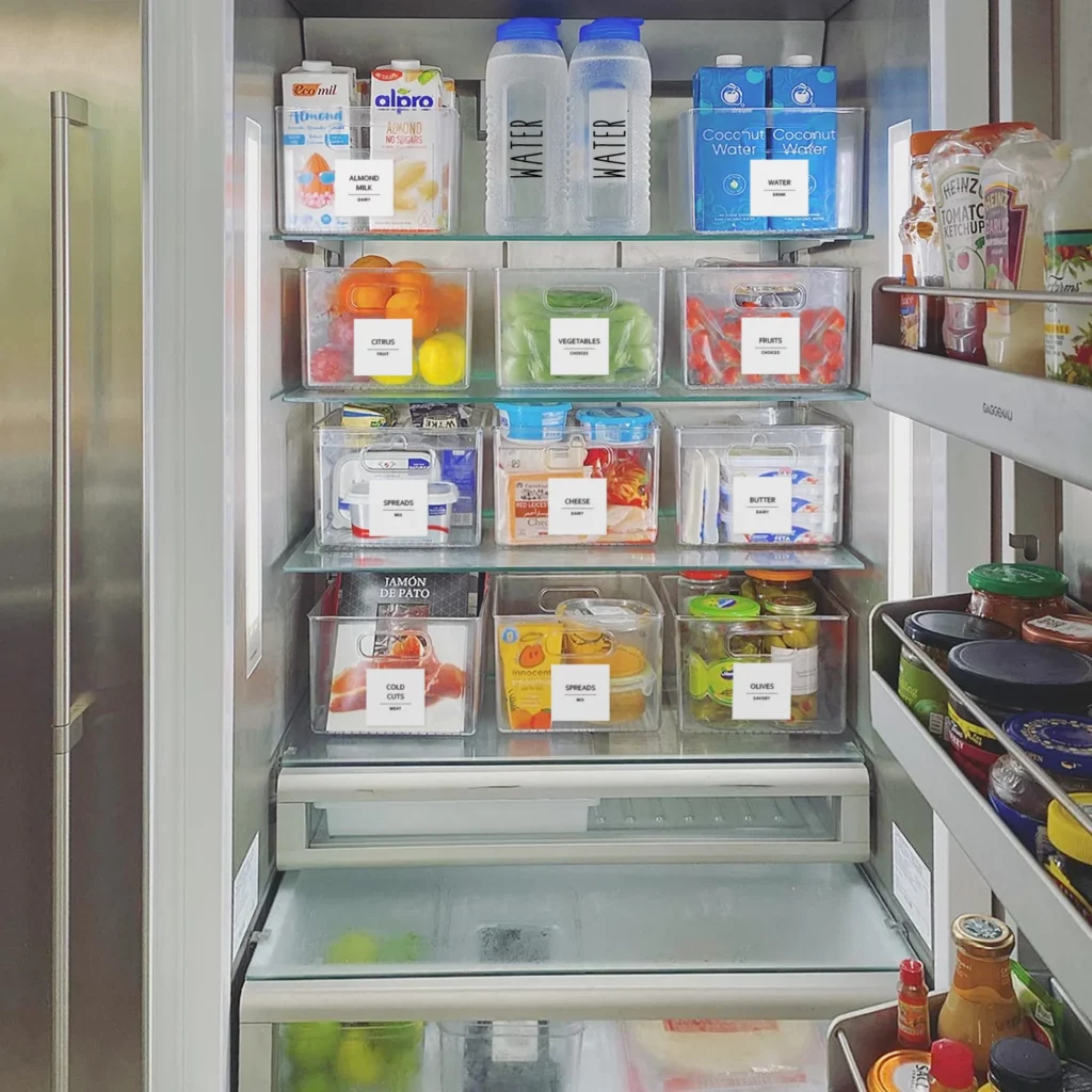 An open refrigerator filled with various food items, including fruits, vegetables, beverages, and other packaged goods, organized on different shelves.
