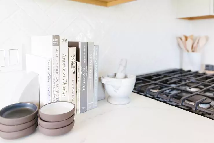 Cookbooks flanked by marble bookends sit on a kitchen countertop beside a marble pestle and mortar.