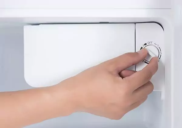 a hand turning on or off a manual defrosting switch in the freezer