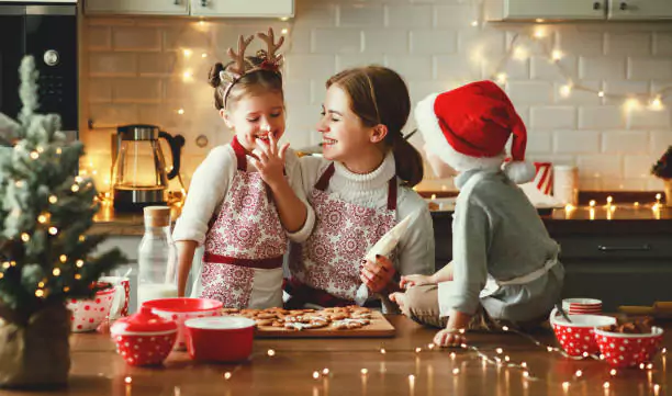 Three children in festive attire are engaging in a holiday baking activity, surrounded by the warm glow of decorative lights, creating a cozy and joyful atmosphere.
