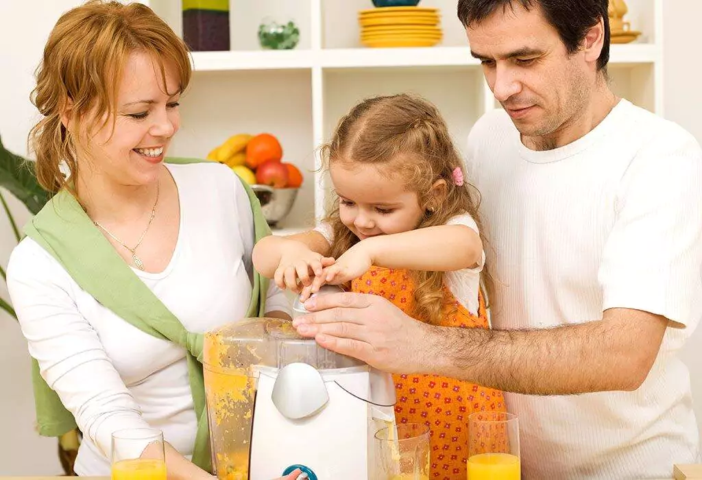 Three people making fresh orange juice using a juicer in a bright kitchen.
