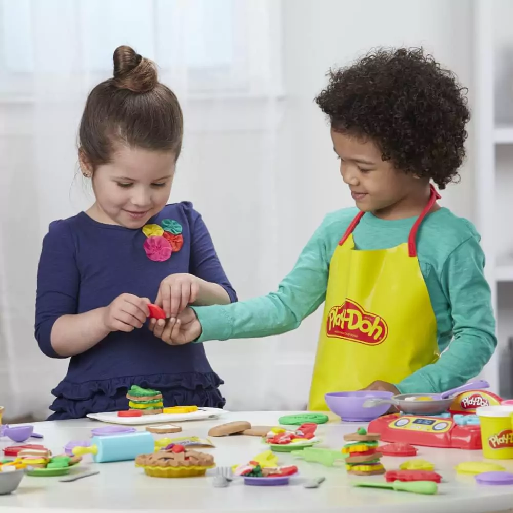 Two children playing with Play-Doh, creating various shapes and objects on a table.
