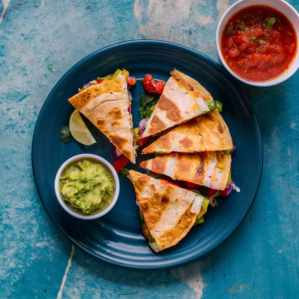 Veggie Quesadillas: Sliced quesadillas with melted cheese and veggies inside, served with salsa and guacamole.