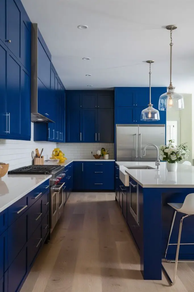 A stunning photograph of a modern kitchen masterfully blending cobalt blue and white, creating a stylish and contemporary space. The cobalt blue cabinetry serves as the focal point, with sleek, flat-panel doors and minimalist chrome handles. White marble or quartz countertops contrast beautifully against the bold cabinets, while a white subway tile backsplash adds a classic touch. A spacious island with matching blue cabinetry and a white countertop features a built-in sink and modern bar stools. Pendant lights with clear glass shades and brushed nickel fixtures hang above the island, illuminating the space with a chic, modern vibe. The light wood flooring adds warmth and balance, while stainless steel appliances seamlessly blend into the design.