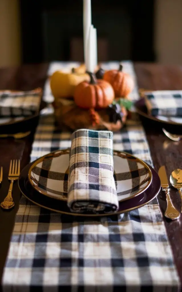 A close-up of a dining table with a plaid theme as part of the fall decor. The tablecloth, runner, and napkins feature plaid patterns, creating a cozy, rustic atmosphere that embodies the spirit of the season.