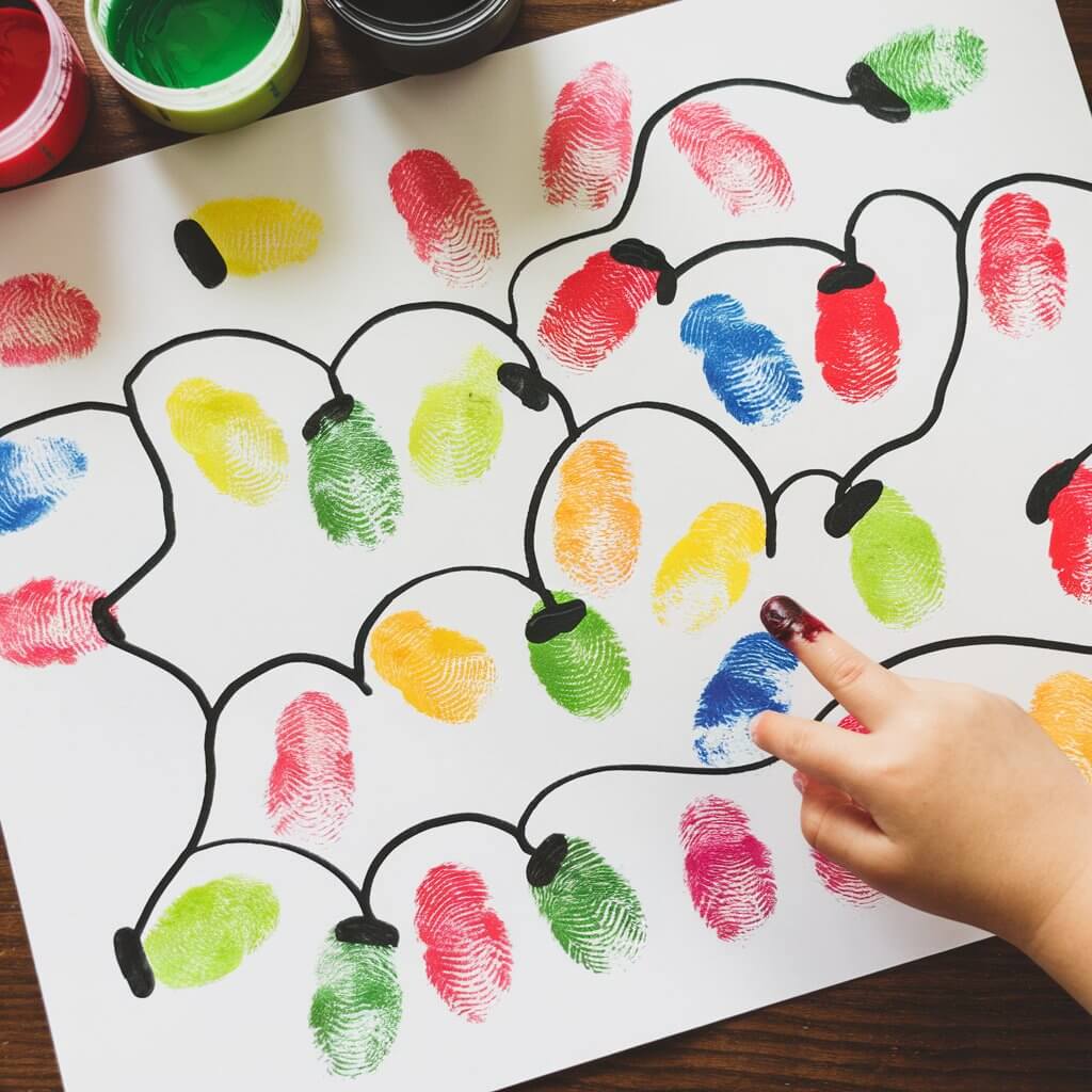 A white paper covered in fingerprint Christmas lights in various bright colors, connected by black marker lines. Small paint containers and a child's finger dipped in paint are visible, illustrating the simple yet festive joy of this fingerprint craft.