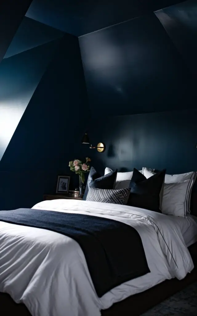 A photo of a dramatic attic bedroom with dark, moody walls painted in deep navy blue. The very cozy bed, with crisp white sheets and dark accent pillows, stands out against the bold backdrop. Soft lighting enhances the room's intimate and cozy feel.