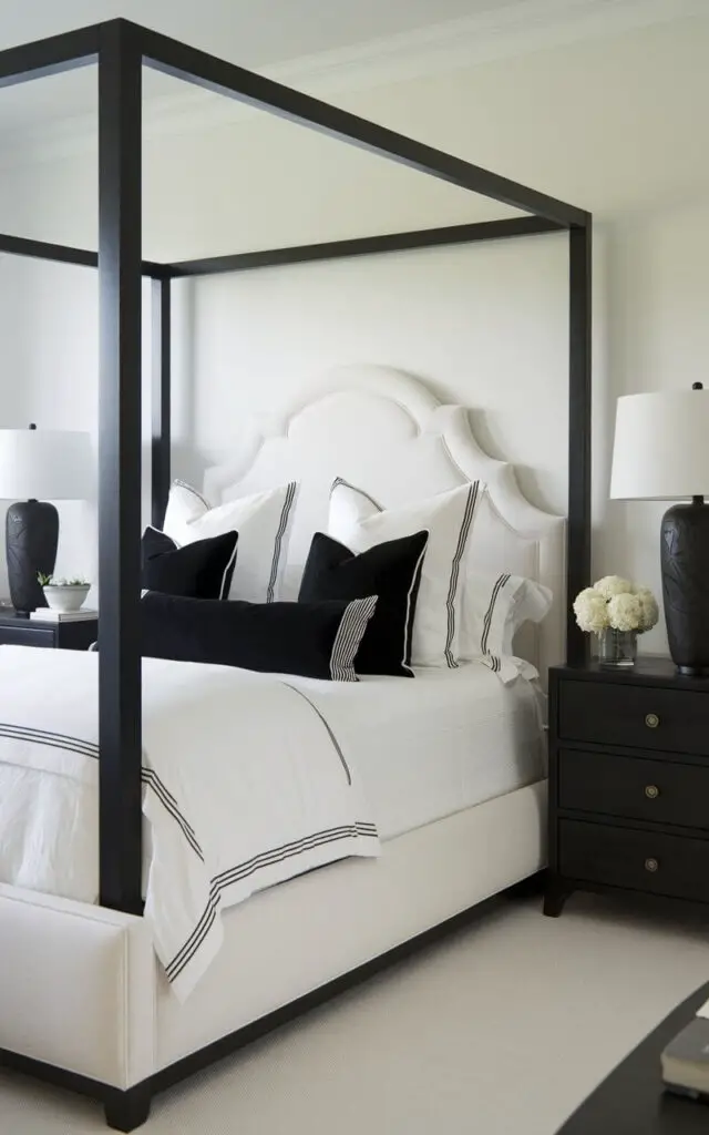 A photo of a black and white bedroom with a cozy bed. The bed has white linens and black accent pillows. The bed's frame is white, making the space bright and airy. Black nightstands with white ceramic lamps are placed on either side of the bed. The lamps add contrast and balance to the serene bedroom.