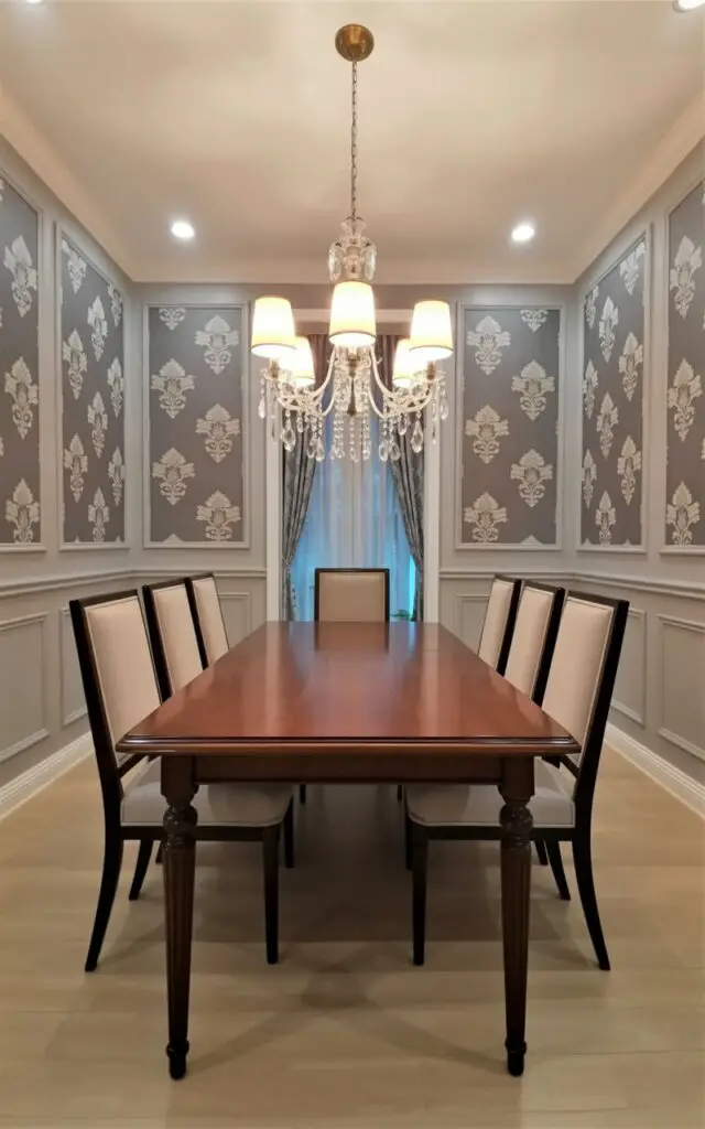 This image presents an elegant dining room wallpaper adorned with a classic damask pattern in soft, tonal shades that evoke timeless sophistication. The room feels like a very well decorate dining room, carefully styled without excess. An empty dining table and dining chairs are positioned symmetrically beneath a refined chandelier, emphasizing balance and order. The minimalist approach keeps furniture silhouettes simple, allowing the intricate wallpaper to shine. Architectural details include paneled walls and a visible Door has a door handle in polished brass, subtly reinforcing the formal yet inviting ambiance of the space.