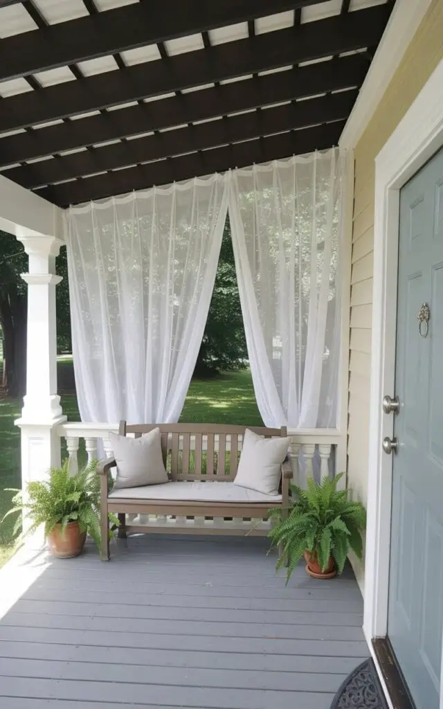 A breezy spring front porch with flowing sheer white outdoor curtains gently moving in the wind. The curtains are mounted along a covered ceiling beam, framing the seating area without overwhelming the space. This very well decorate front porch maintains a minimalist aesthetic—light neutral cushions, a simple wooden bench, and subtle potted greenery arranged symmetrically. The focal entry door, painted pale blue, stands at the center; the door has a keyhole and a handle in brushed nickel, both crisp and refined in detail. Sunlight filters softly through the translucent fabric, casting delicate shadows that add movement and serenity.